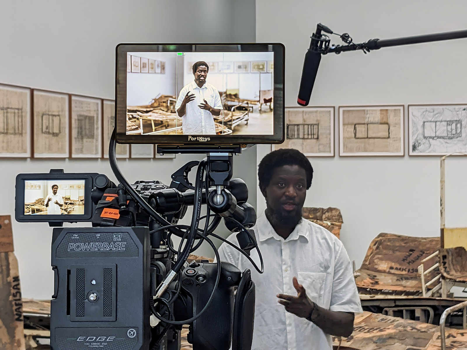 BTS interview with an artist in a gallery. The set includes a camera with two monitors and a microphone boom.